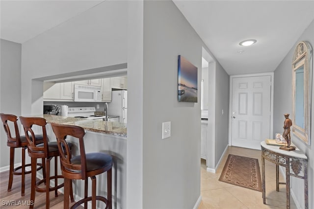 kitchen with a kitchen breakfast bar, light stone counters, white appliances, light tile patterned floors, and white cabinets