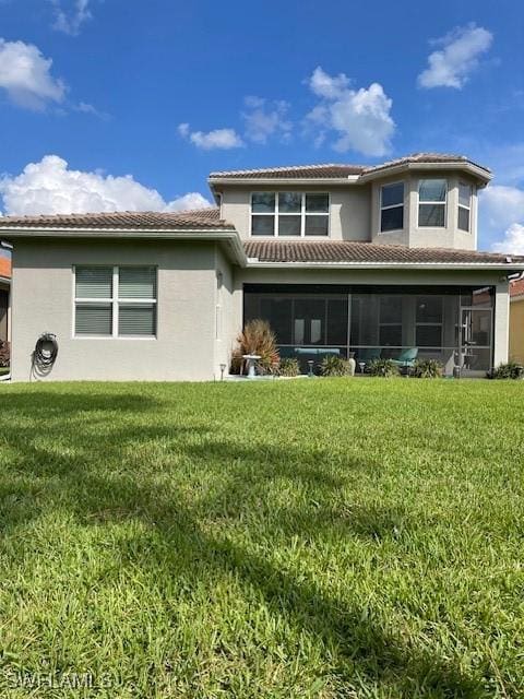 rear view of property featuring a tiled roof, a sunroom, a lawn, and stucco siding