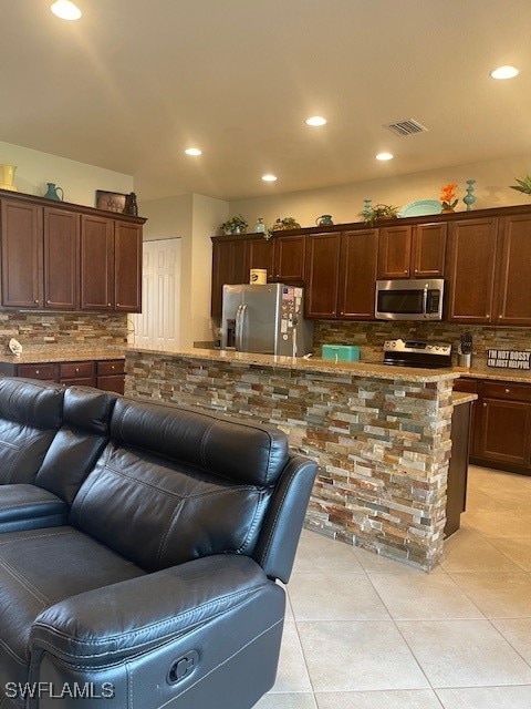 kitchen featuring dark brown cabinetry, tasteful backsplash, stone countertops, light tile patterned floors, and stainless steel appliances