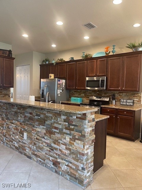 kitchen featuring appliances with stainless steel finishes, decorative backsplash, light tile patterned flooring, and light stone countertops