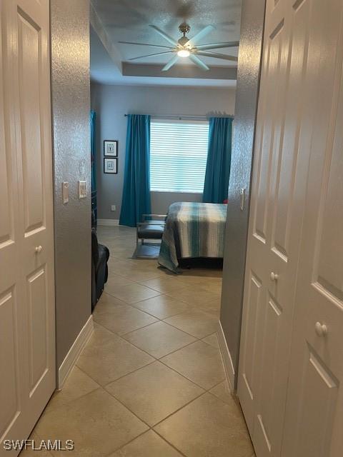 hall featuring baseboards, a tray ceiling, and light tile patterned flooring