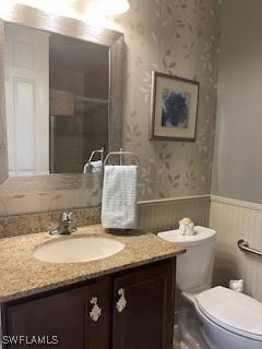 bathroom featuring toilet, wallpapered walls, a wainscoted wall, and vanity