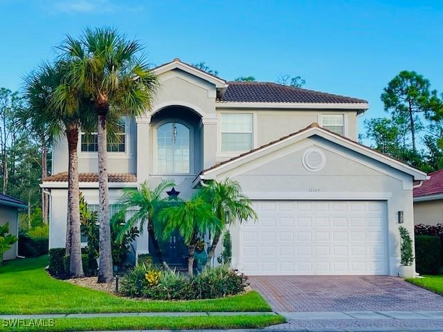 mediterranean / spanish home featuring stucco siding, a tiled roof, decorative driveway, and a front lawn