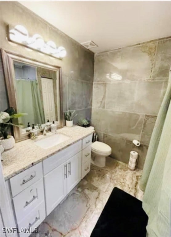 bathroom featuring a shower with curtain, toilet, vanity, tile patterned floors, and tile walls