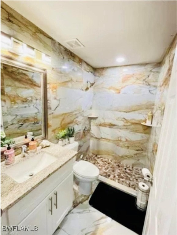 bathroom with tile patterned flooring, a tile shower, vanity, and toilet