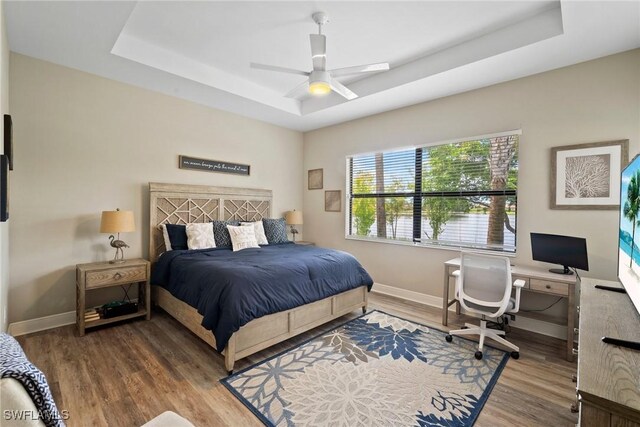 bedroom with ceiling fan, hardwood / wood-style flooring, and a tray ceiling