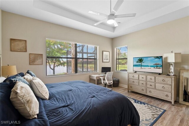 bedroom with ceiling fan, light hardwood / wood-style flooring, and a raised ceiling