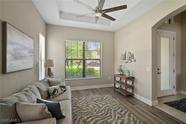 sitting room with wood-type flooring, ceiling fan, and a raised ceiling