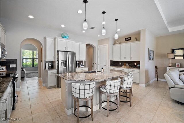 kitchen with white cabinets, an island with sink, hanging light fixtures, sink, and appliances with stainless steel finishes