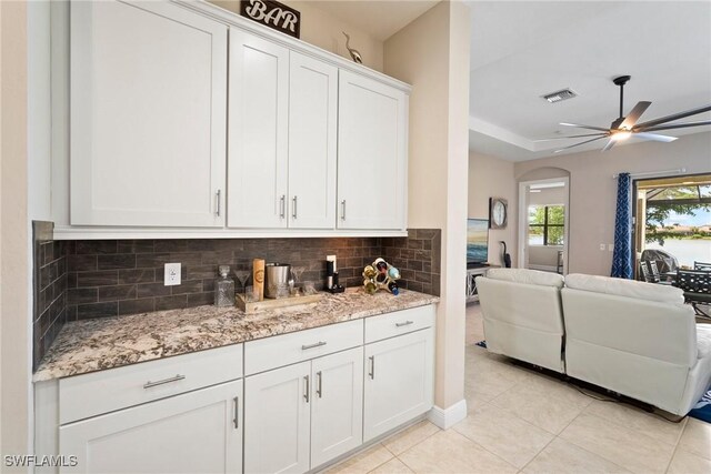 kitchen featuring ceiling fan, light tile patterned flooring, white cabinetry, light stone countertops, and decorative backsplash