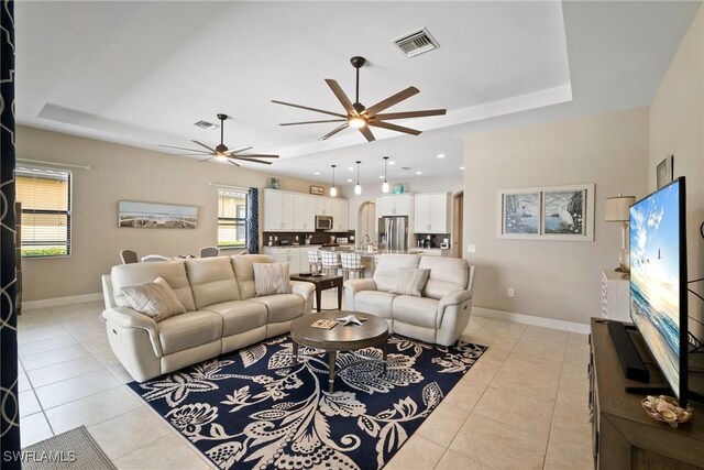 living room featuring ceiling fan, sink, a raised ceiling, and light tile patterned floors