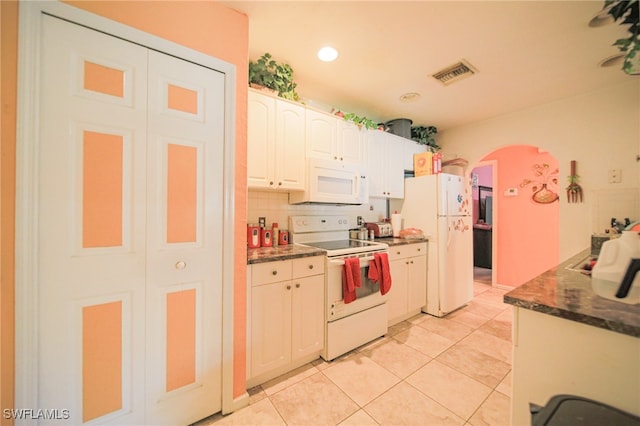 kitchen featuring white appliances, light tile patterned floors, tasteful backsplash, white cabinetry, and dark stone counters