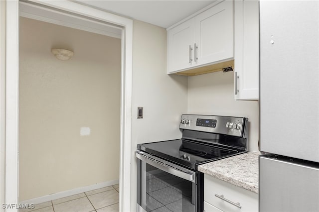 kitchen featuring light tile patterned floors, electric range, baseboards, freestanding refrigerator, and white cabinetry