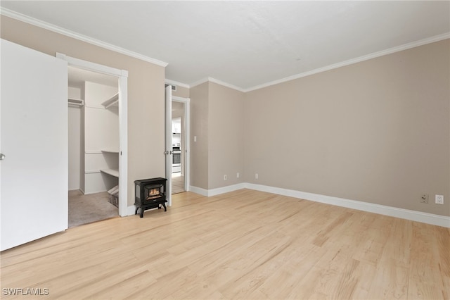 unfurnished bedroom featuring crown molding, light wood-style flooring, a spacious closet, a wood stove, and baseboards