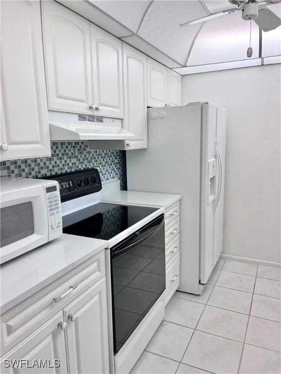 kitchen with white cabinets, under cabinet range hood, light tile patterned floors, and white appliances