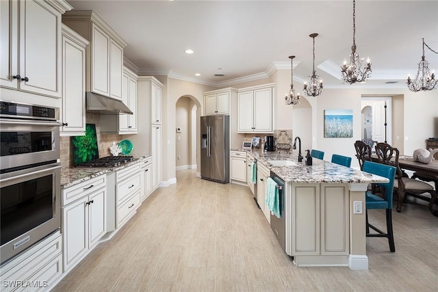 kitchen featuring sink, a breakfast bar area, hanging light fixtures, light stone counters, and stainless steel appliances