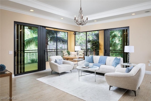 living room with a notable chandelier, ornamental molding, light wood-type flooring, and a raised ceiling