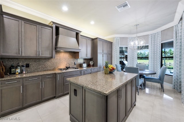 kitchen featuring a notable chandelier, pendant lighting, a kitchen island, custom exhaust hood, and ornamental molding