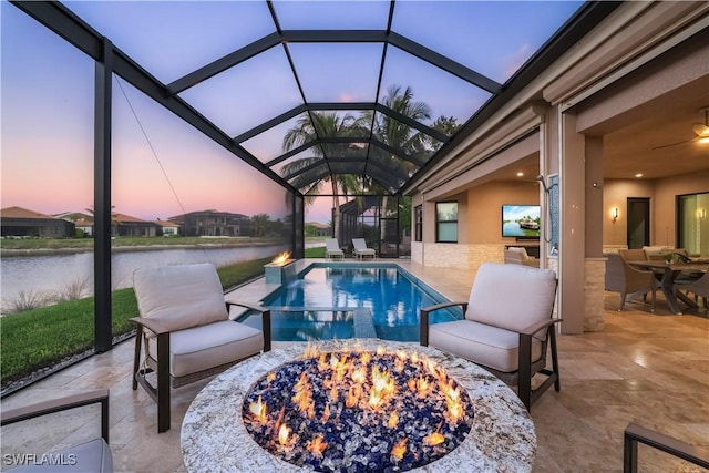 pool at dusk featuring glass enclosure, a water view, an outdoor fire pit, and a patio