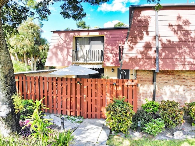 back of house featuring a fenced front yard, a balcony, and brick siding