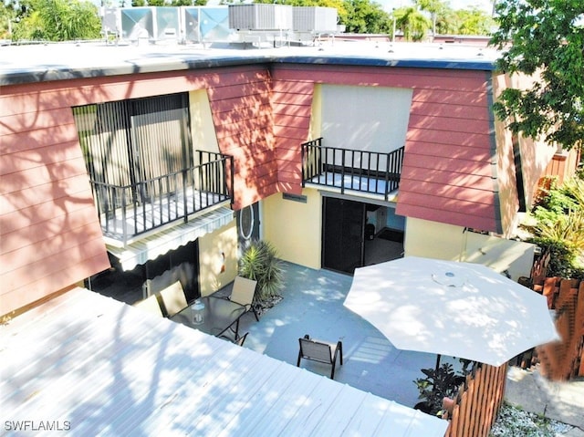 rear view of property featuring outdoor dining area, a balcony, and stucco siding