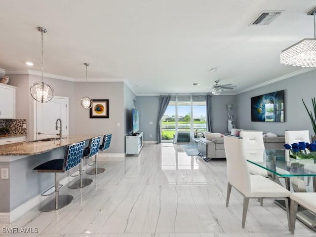 dining space with ceiling fan with notable chandelier, ornamental molding, and sink