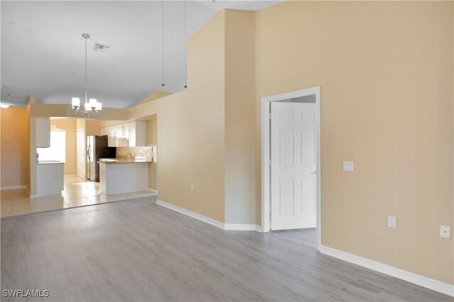 unfurnished living room with lofted ceiling, a chandelier, and light hardwood / wood-style floors