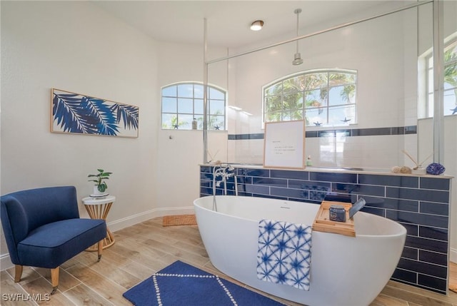 bathroom with wood finish floors, a freestanding tub, and a healthy amount of sunlight