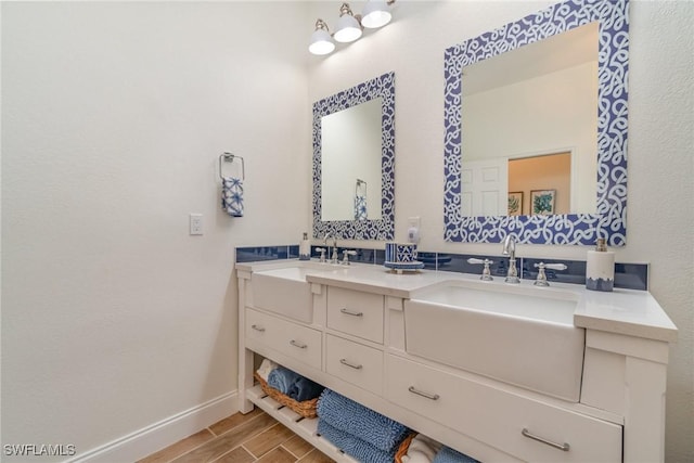 bathroom with wood finish floors, a sink, baseboards, and double vanity