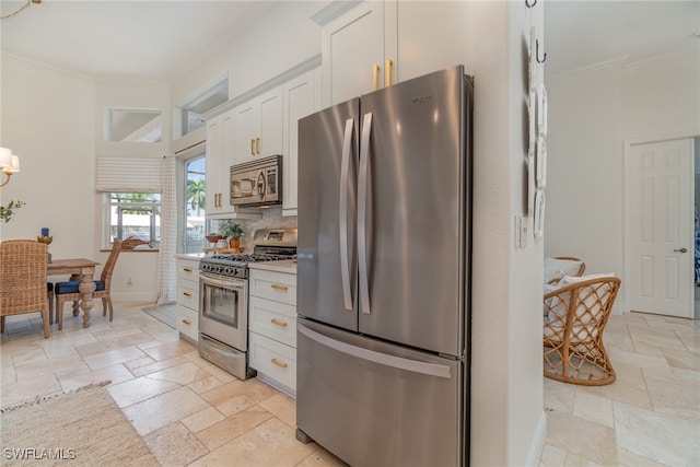 kitchen with stainless steel appliances, stone tile flooring, light countertops, ornamental molding, and white cabinetry