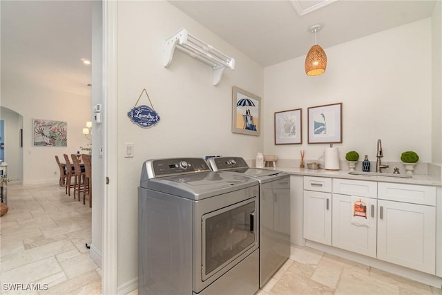 laundry area featuring cabinet space, arched walkways, stone tile flooring, washer and dryer, and a sink