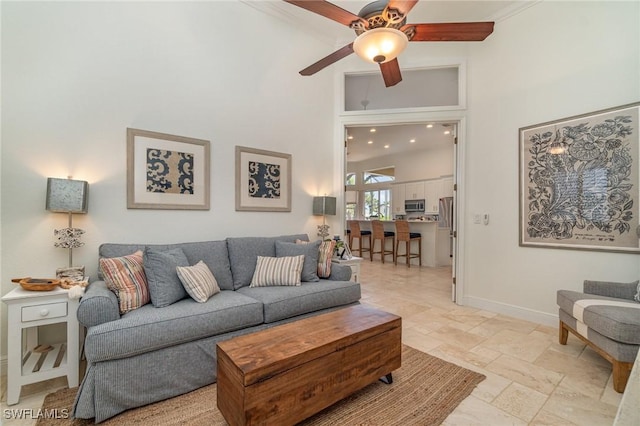 living room with a ceiling fan, stone tile flooring, a towering ceiling, and baseboards