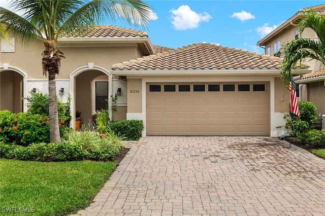 mediterranean / spanish home with a garage, decorative driveway, a tile roof, and stucco siding