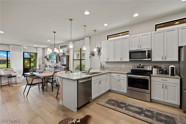 kitchen featuring kitchen peninsula, light stone countertops, appliances with stainless steel finishes, decorative light fixtures, and white cabinetry