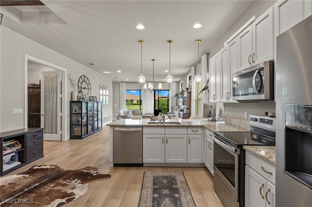 kitchen featuring white cabinets, a peninsula, hanging light fixtures, stainless steel appliances, and light wood-style floors