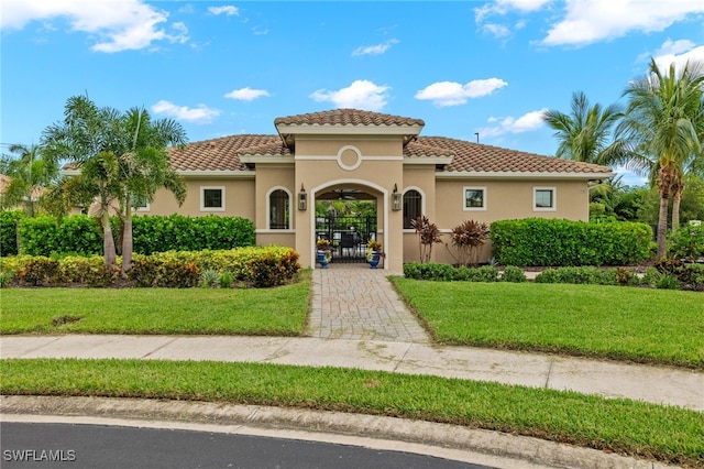 mediterranean / spanish-style house with a gate, a tile roof, a front lawn, and stucco siding