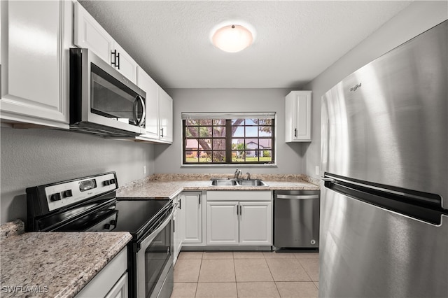 kitchen with appliances with stainless steel finishes, white cabinetry, sink, light stone countertops, and light tile patterned floors