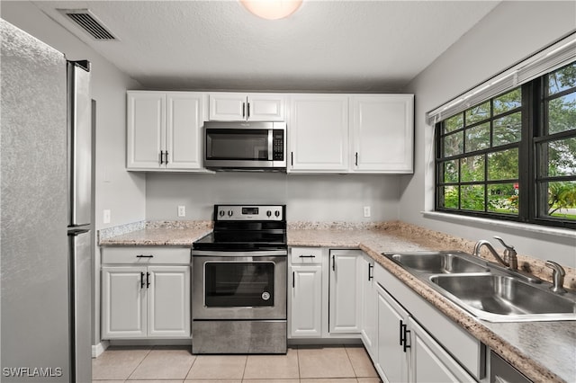 kitchen with light tile patterned floors, sink, stainless steel appliances, and white cabinets