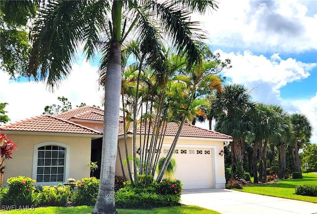 mediterranean / spanish home with a garage, driveway, stucco siding, a tile roof, and a front yard