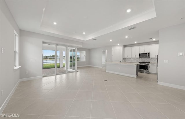 unfurnished living room featuring light tile patterned flooring, a tray ceiling, and sink