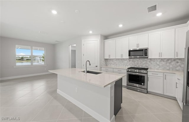 kitchen with sink, appliances with stainless steel finishes, white cabinetry, light stone counters, and a center island with sink