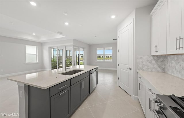 kitchen with appliances with stainless steel finishes, white cabinetry, an island with sink, sink, and light stone countertops