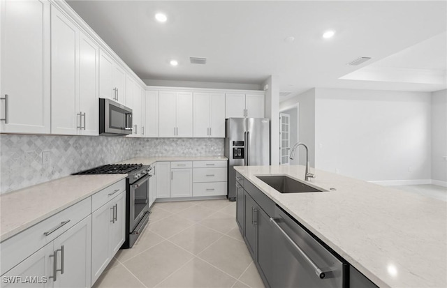 kitchen with sink, appliances with stainless steel finishes, white cabinetry, light stone counters, and light tile patterned flooring