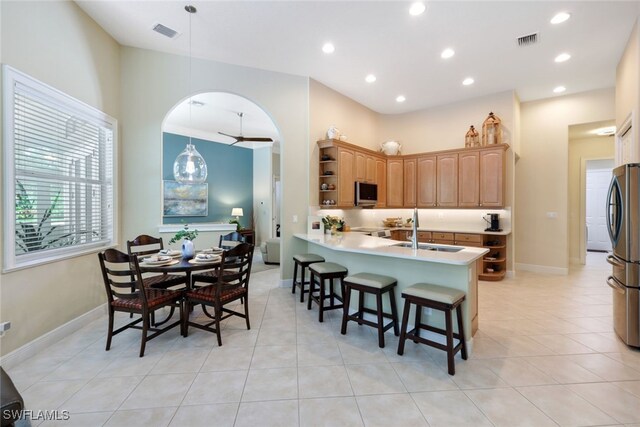 kitchen featuring stainless steel appliances, sink, light tile patterned floors, kitchen peninsula, and a breakfast bar area