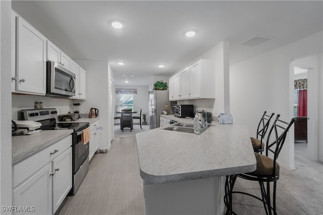 kitchen with a kitchen bar, appliances with stainless steel finishes, white cabinetry, kitchen peninsula, and light colored carpet