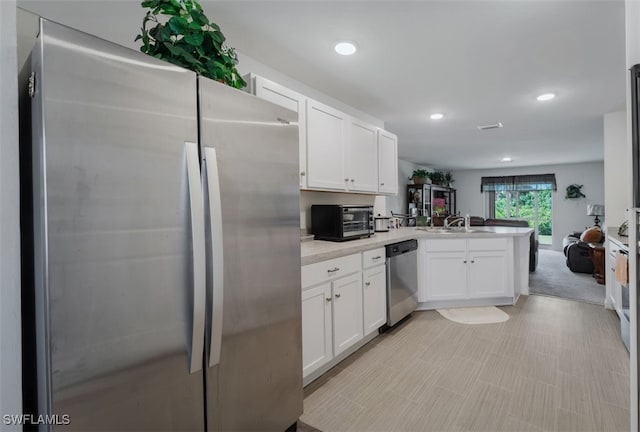 kitchen featuring stainless steel appliances, sink, white cabinets, light colored carpet, and kitchen peninsula