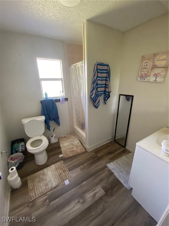 bathroom featuring toilet, hardwood / wood-style floors, a textured ceiling, vanity, and walk in shower