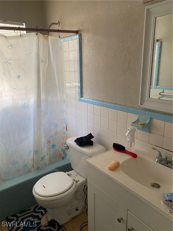 full bathroom with tile walls, vanity, toilet, and shower / tub combo with curtain