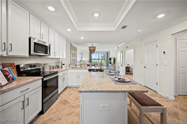 kitchen with appliances with stainless steel finishes, ornamental molding, a kitchen bar, light stone counters, and a raised ceiling