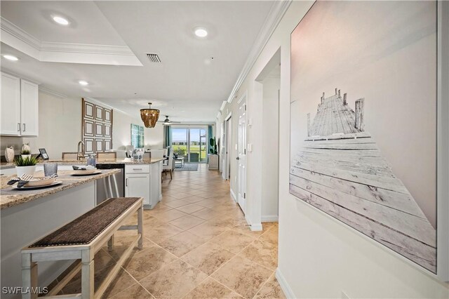 kitchen with light tile patterned floors, light stone countertops, a tray ceiling, white cabinetry, and crown molding